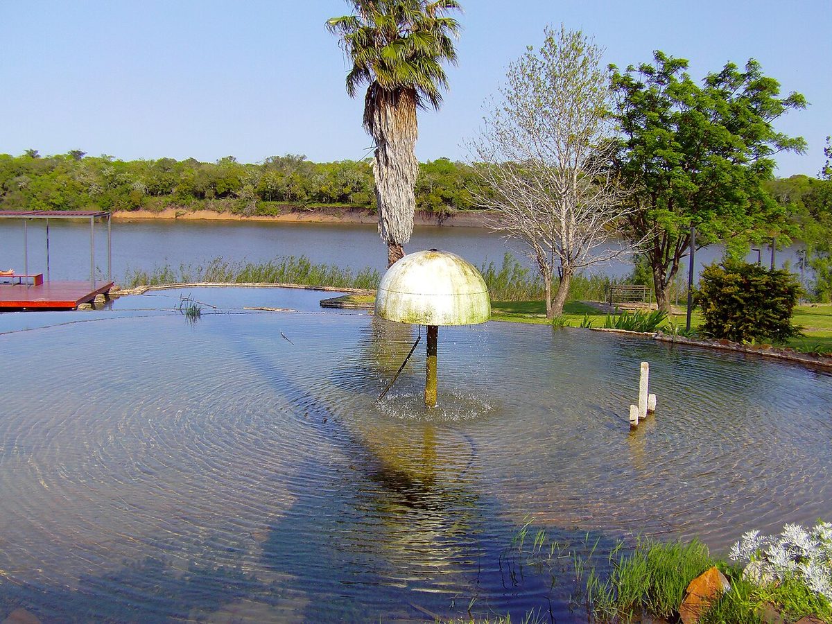 An open-air thermal pool ringed by green lawns and palm trees at Arapey, Uruguay