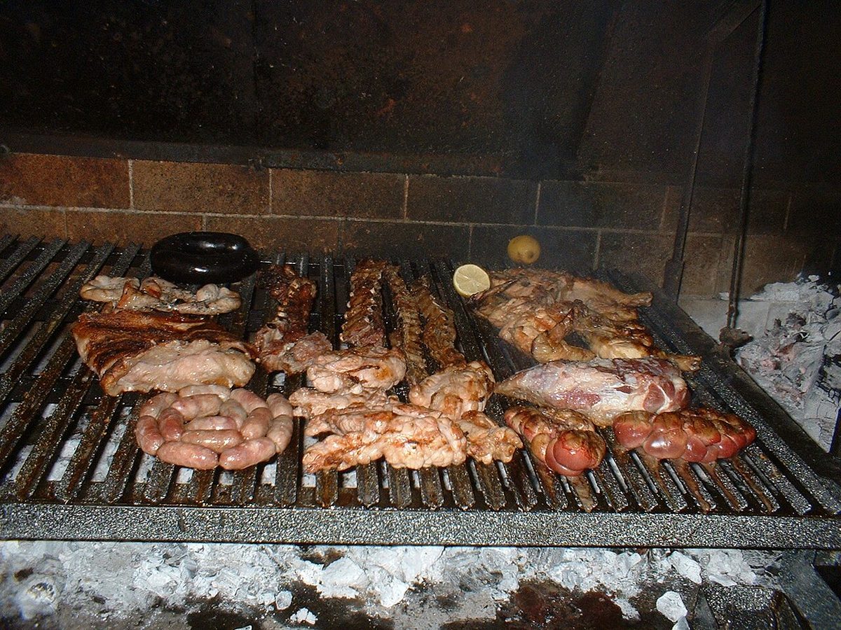 Beef cuts and chorizo grilling over wood embers on a traditional parrilla — asado culture is one thing Argentina and Uruguay genuinely share