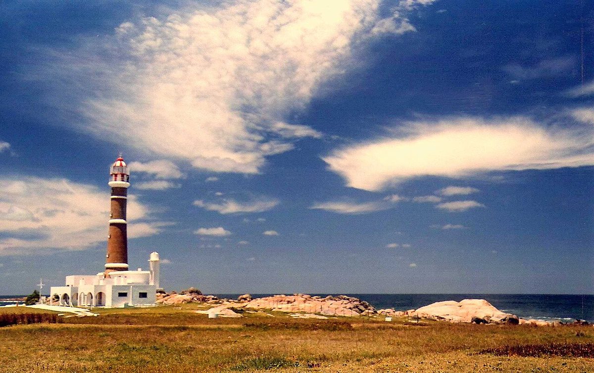 The lighthouse at Cabo Polonio rising over the headland with sea lions on the rocks below