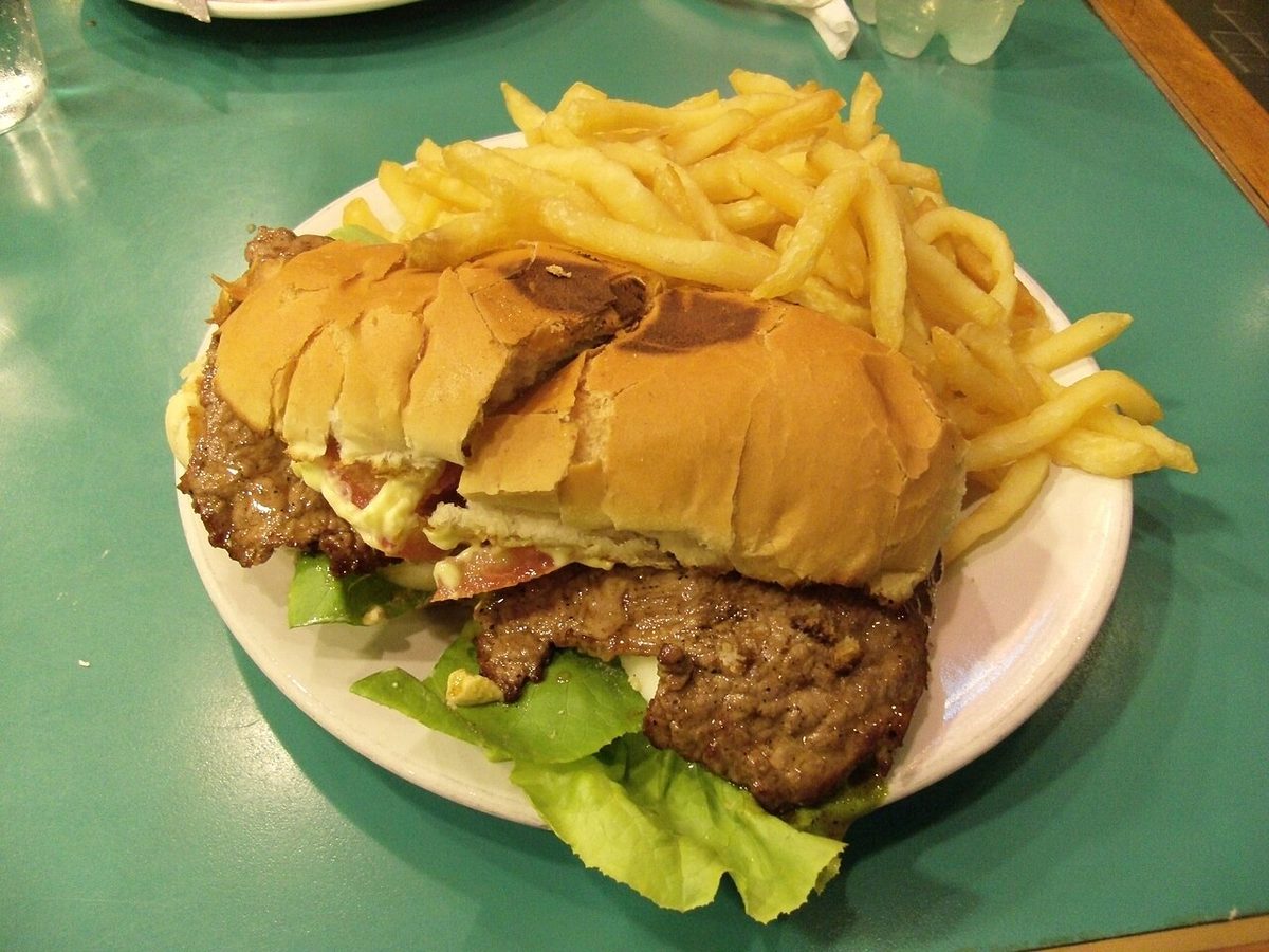 A fully loaded steak sandwich with bacon, ham, melted cheese and a fried egg served with chips
