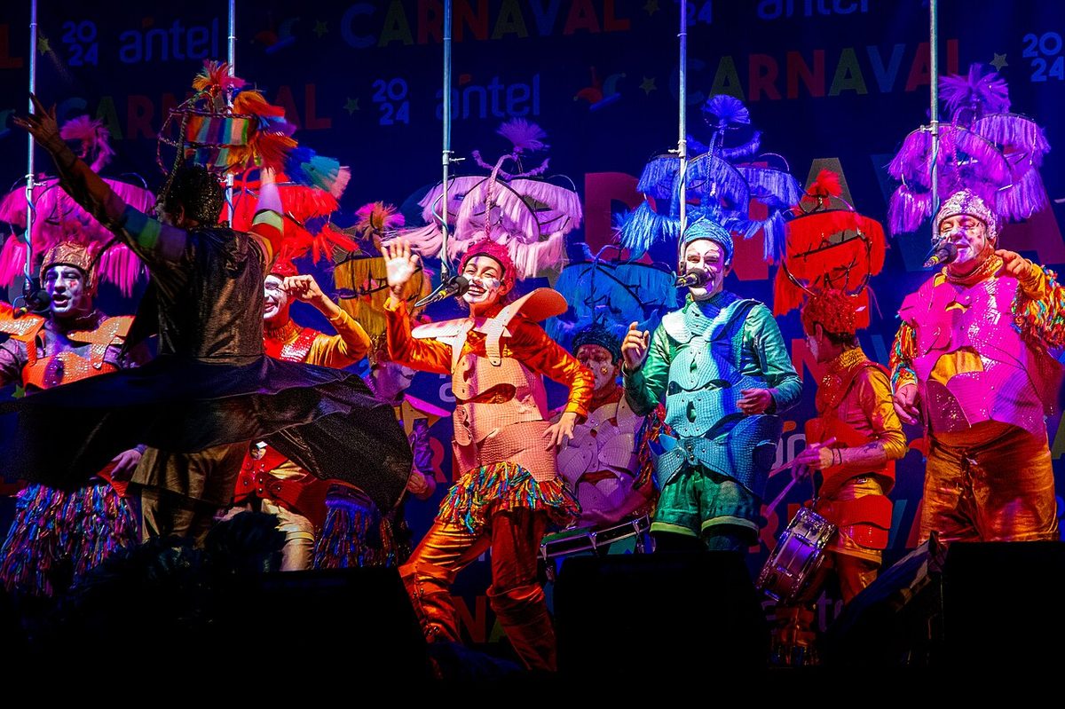 The three murga percussionists playing bombo bass drum, platillos cymbals and redoblante snare at the side of the stage
