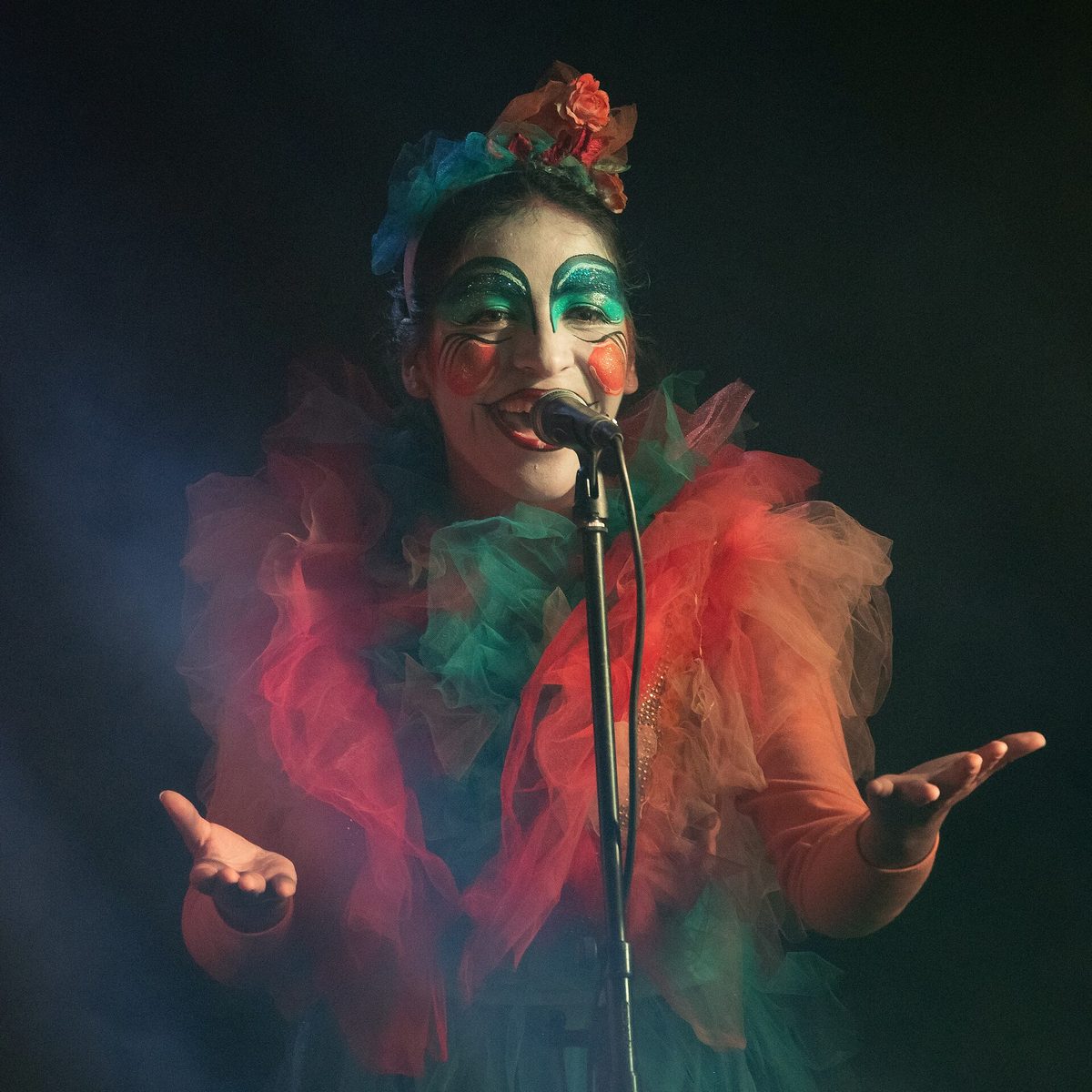 A murga performer in a bright costume and full face paint singing on stage during Uruguayan Carnival