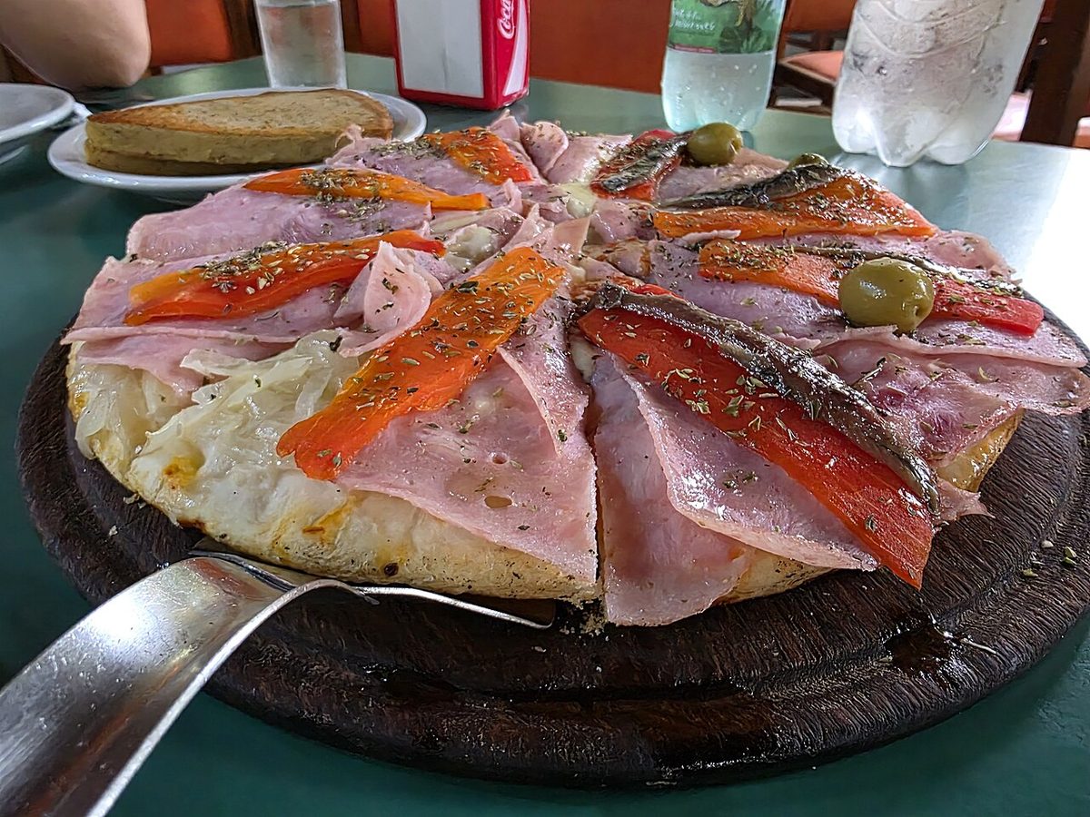 Slice of square Uruguayan pizza topped with faina chickpea flatbread