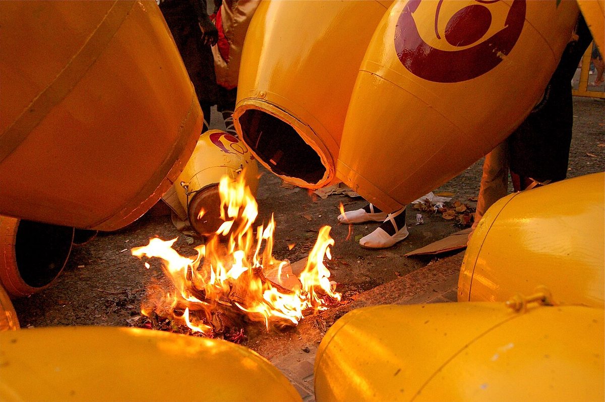 A drummer tuning the lonja of a tamboril over a street fire before playing