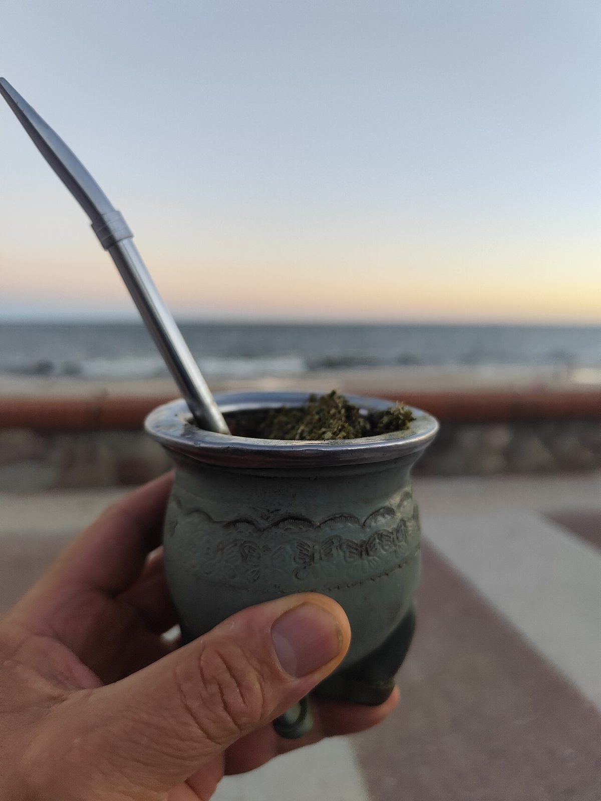 A person drinking mate uruguay style on the Montevideo Rambla, gourd in hand and thermos under the arm