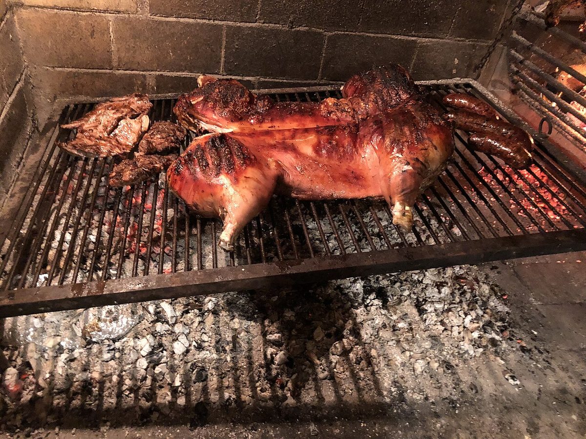 A Uruguayan parrilla grill with cuts of beef cooking over wood coals for an asado